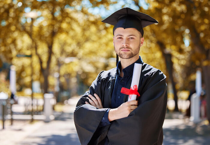 Young man in graduation gown holding diploma, symbolizing most likely to succeed amid surprising plot twists outdoors.