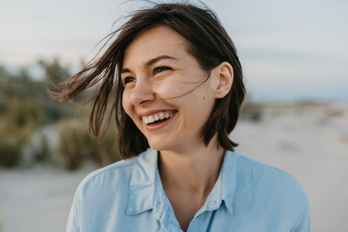 Young woman smiling outdoors with wind blowing through her hair, illustrating small tricks that make being a grown-up easier.