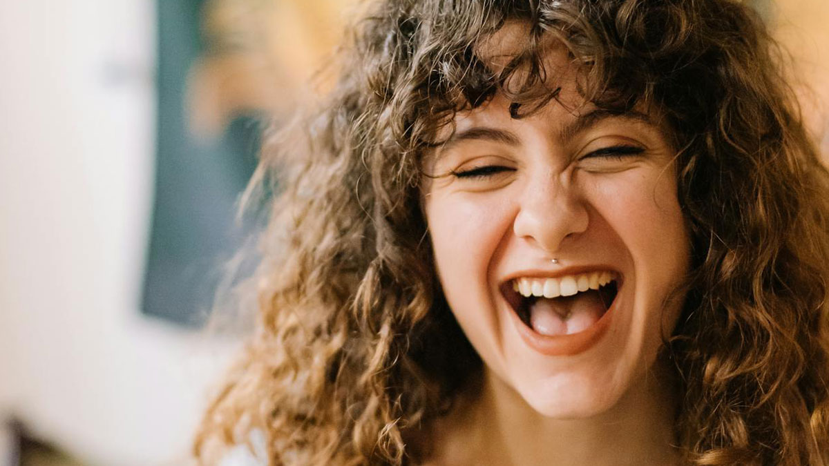 Young woman with curly hair laughing joyfully, capturing the spirit of brilliantly sneaky acts of revenge.