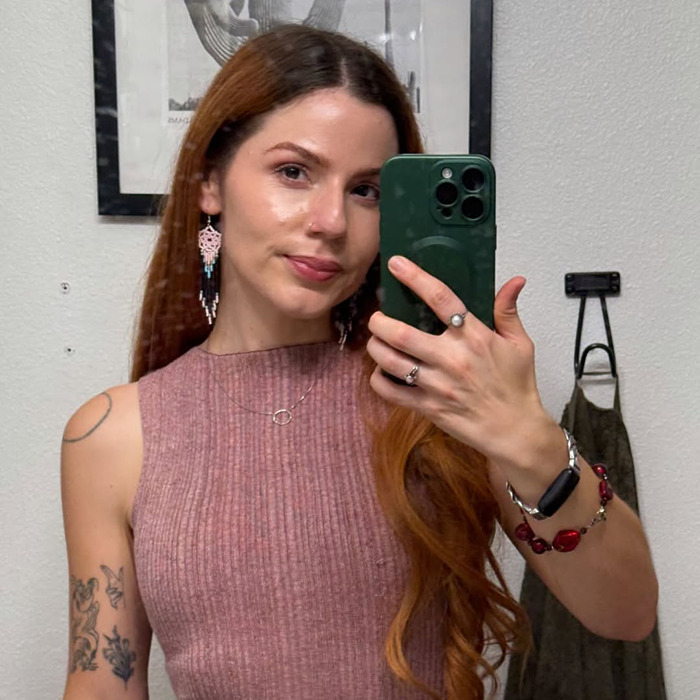 Young woman taking a selfie while wearing a pink sleeveless top, showcasing tattoos and long reddish hair for social media post. Young woman taking a selfie while wearing a pink sleeveless top, showcasing tattoos and long reddish hair for social media post.