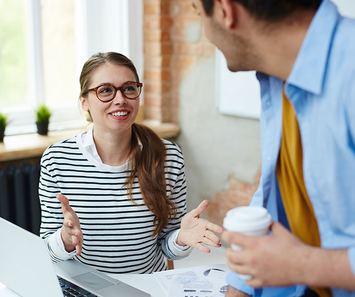 Young woman smiling and sharing psychological cheat codes with a colleague to make social life easier in an office setting.