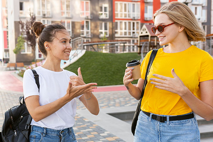 Two women smiling and using psychological cheat codes while enjoying a casual social interaction outdoors.