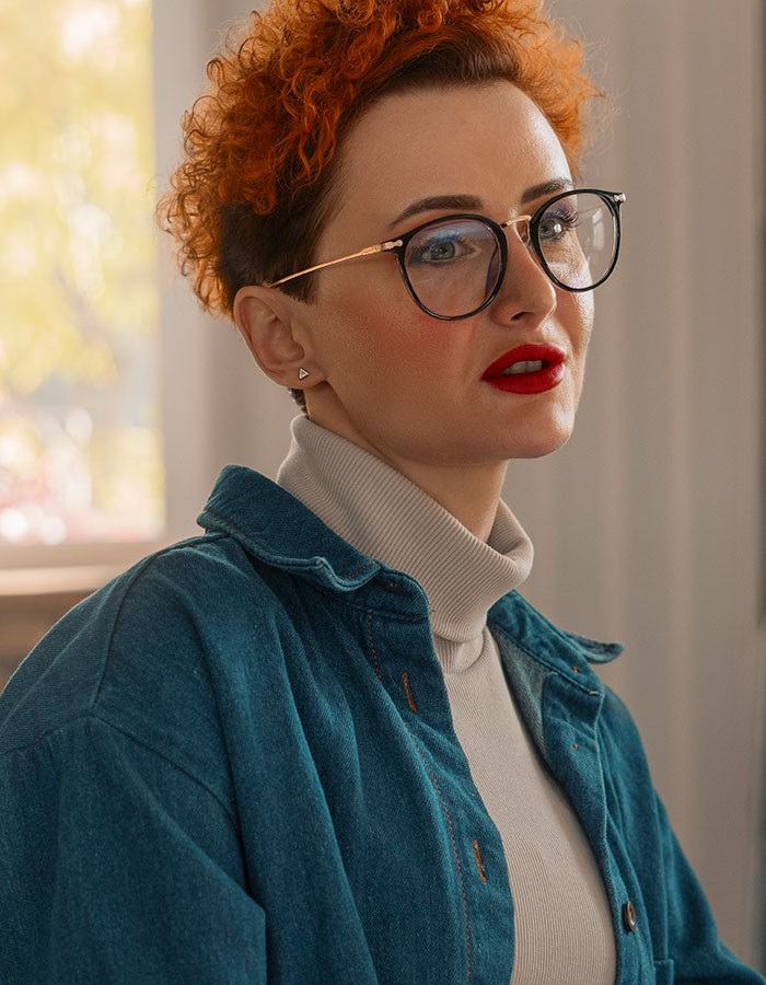 Person with curly red hair and glasses wearing denim jacket, representing psychological cheat codes for easier social life.