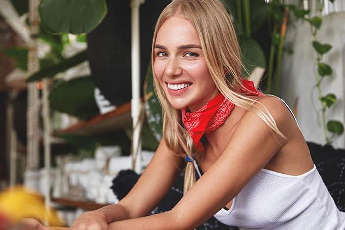 Young woman smiling indoors surrounded by plants, illustrating psychological cheat codes for easier social life.