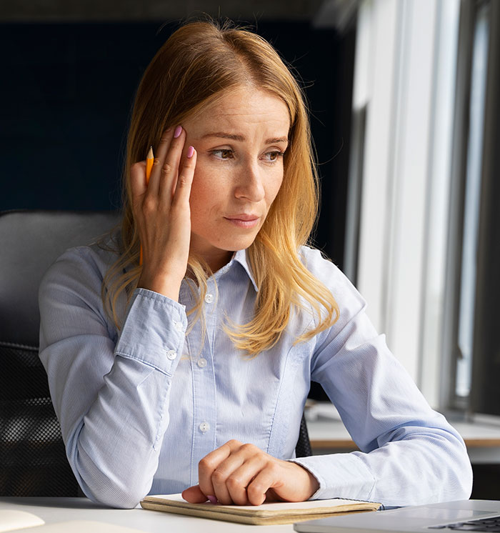 Woman in light blue shirt holding pencil and looking thoughtful, illustrating psychological cheat codes for easier social life.