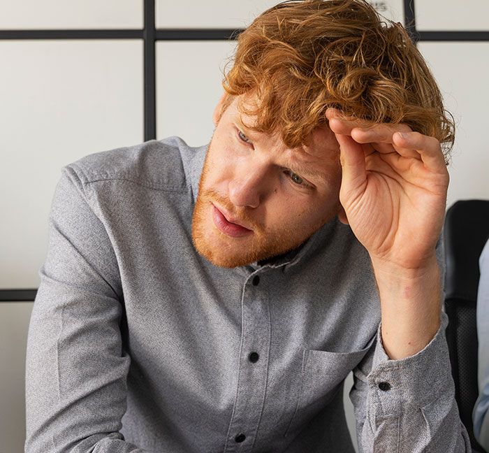 Young man with red hair and beard looks thoughtful while touching his forehead, illustrating psychological cheat codes for social life.