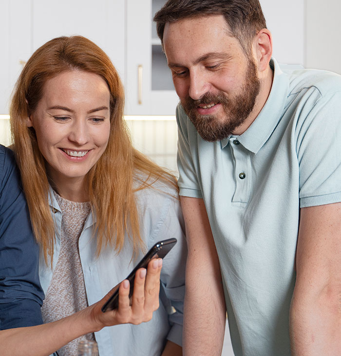 Two people smiling and looking at a phone, demonstrating psychological cheat codes in social situations.