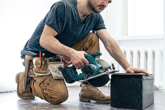 Man wearing casual clothes using a circular saw while kneeling on the floor, illustrating psychological cheat codes in action.