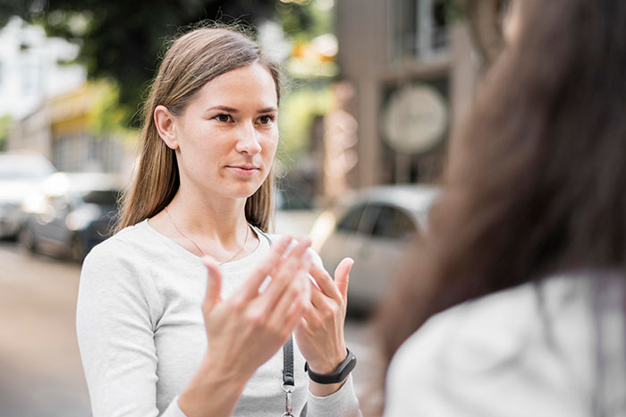 Young woman using psychological cheat codes during a conversation with another person on a city street.