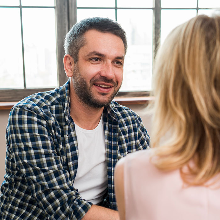 Man smiling and talking to woman in a bright room, illustrating psychological cheat codes for easier social life.