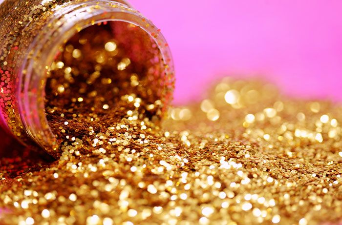 Close-up of golden glitter spilling from a jar on a pink background, representing diabolical revenge stories visually.