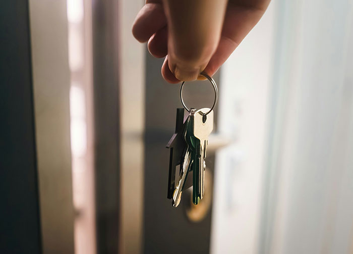 Hand holding house keys near a door lock, illustrating diabolical revenge stories and unwanted enemies concept.