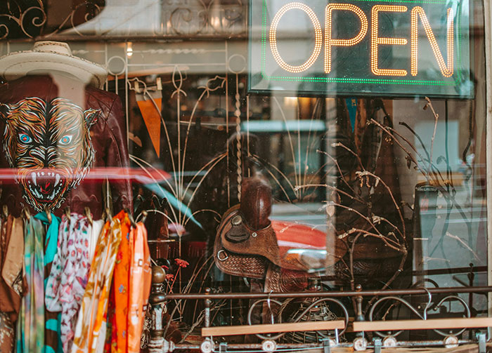Shop window with colorful clothes, leather jackets, and a neon open sign reflecting street scene, capturing revenge stories vibe.