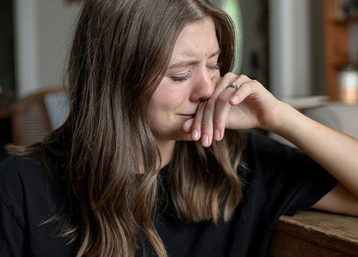 Young woman with long hair crying and covering mouth with hand, conveying intense emotion in a diabolical revenge story context.