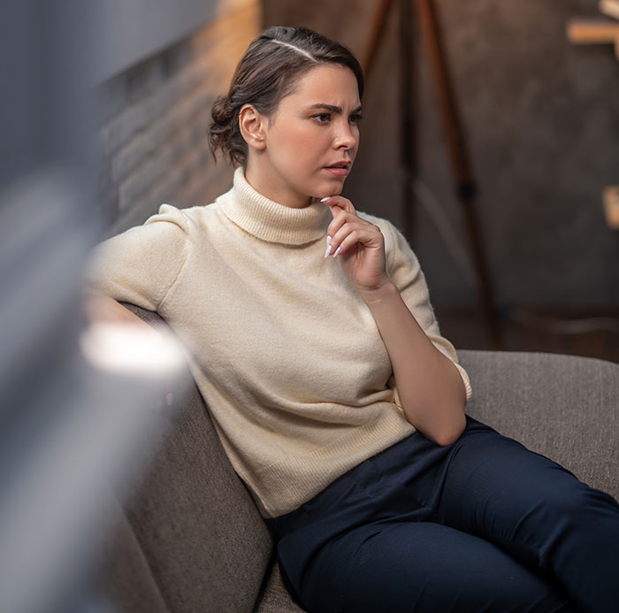 Young woman sitting on couch with a panic on her face, showing serious concern while listening intently in a cozy room.