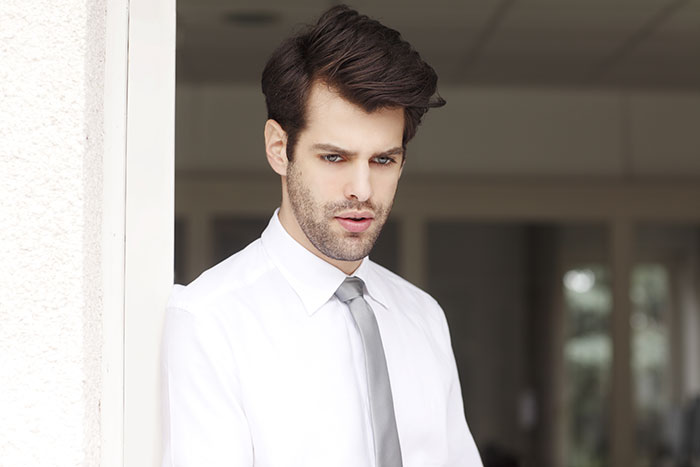 Young businessman with panic on his face, wearing white shirt and tie, standing near doorway in an office setting.