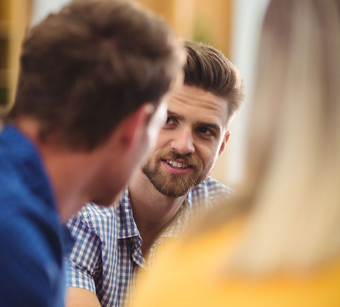 Young man showing panic on his face while talking seriously with others in a casual indoor setting