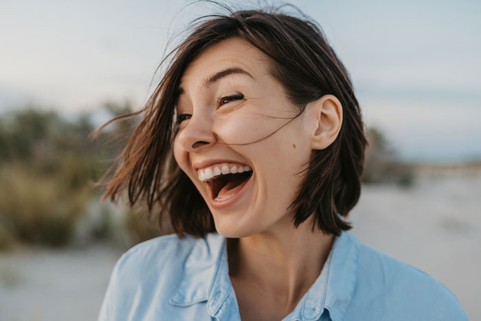 Young woman smiling outdoors with wind blowing hair, showing unexpected emotion contrasting panic on his face theme.