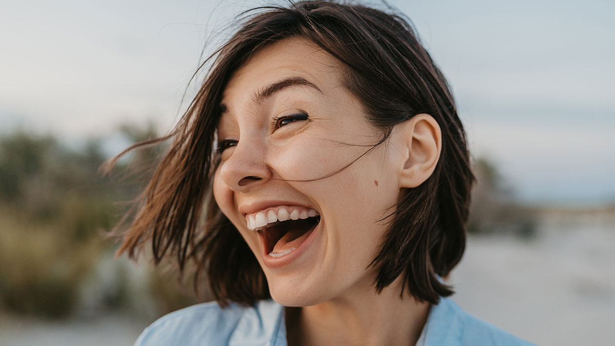Young woman laughing outdoors, showing a lighthearted moment contrasting with panic expressions in serious situations