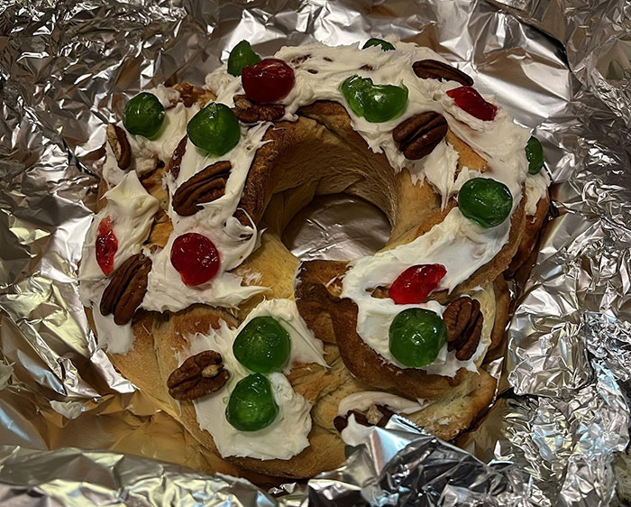 Homemade Christmas bread decorated with pecans, green and red candied cherries wrapped in foil on a dark surface.