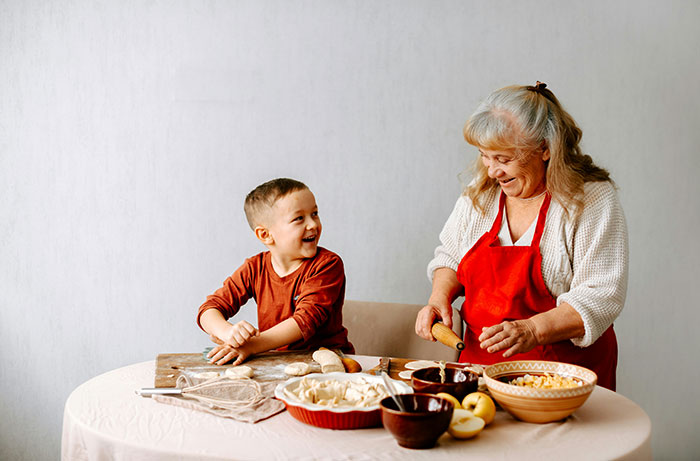 Grandmother and child preparing homemade pies together at a table filled with baking ingredients and utensils.
