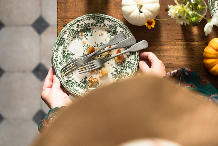 Person holding an empty plate with crumbs and forks, symbolizing homemade pies eaten behind their back.
