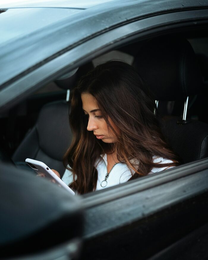 Young woman inside a car looking at her phone, illustrating instant karma and reminders to be on your best behavior.