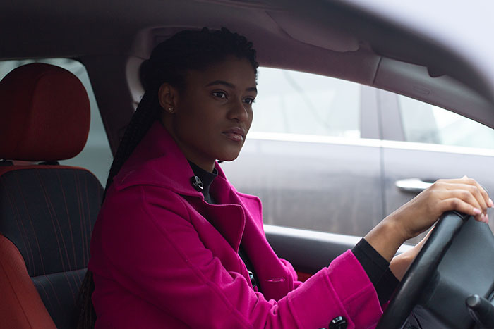 Woman in a magenta coat driving a car, capturing a moment from things people never took seriously until experienced themselves.