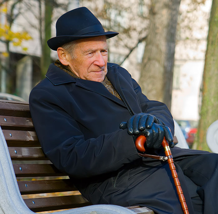 Elderly man with cane sitting on bench outdoors, reflecting on things people never took seriously until experienced.