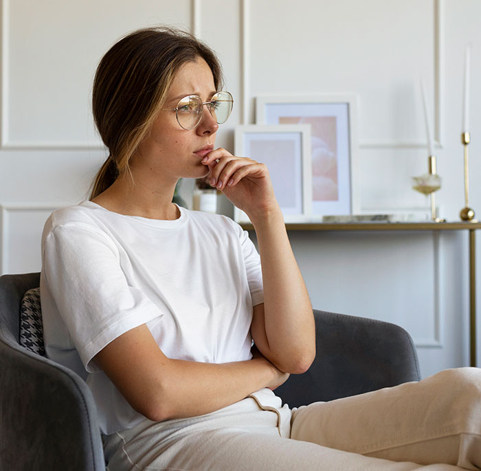 Young woman wearing glasses sitting thoughtfully in a chair, reflecting on things people never took seriously until experienced.