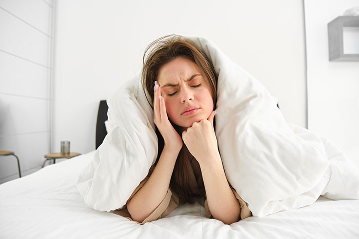 Young woman experiencing stress and discomfort in bed wrapped in a blanket, showing things people never took seriously until they experienced them
