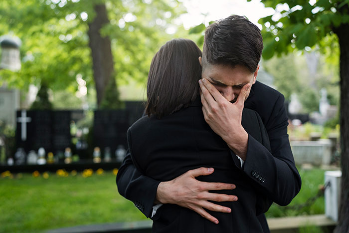 Man visibly emotional and hugging a woman at a cemetery, reflecting on things people only believe once experienced.