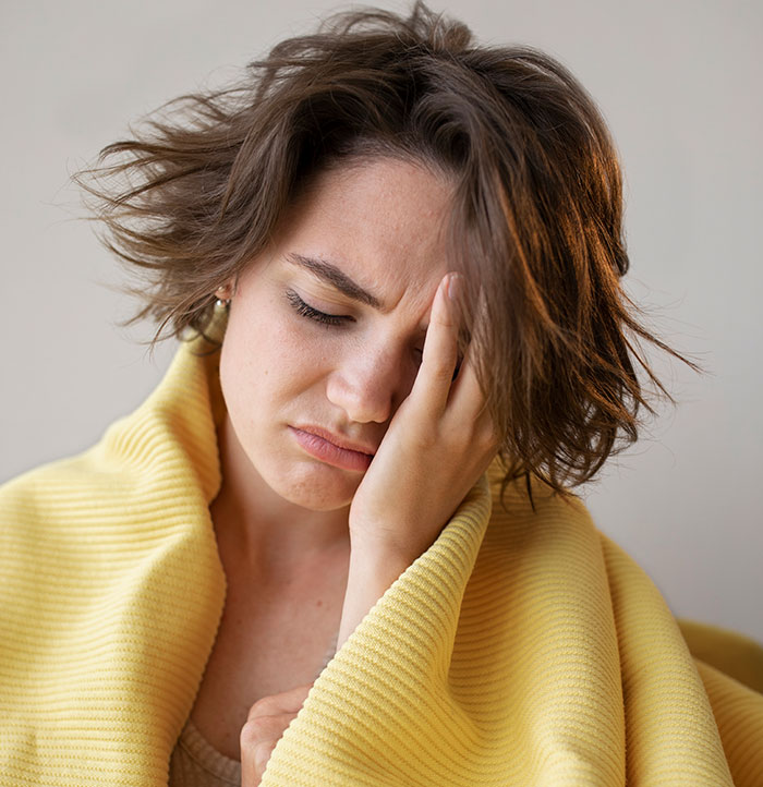 Young woman wrapped in a yellow blanket holding her head, illustrating things people only started to believe once it happened to them