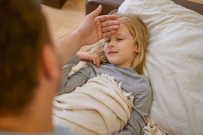 Child lying in bed while an adult checks her forehead, illustrating things people only believe once it happens to them.