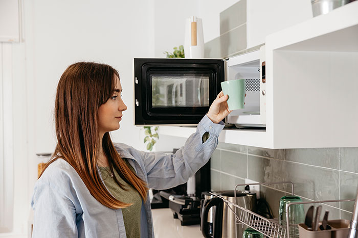 Woman using a microwave in a kitchen, illustrating everyday moments people only start to believe once experienced.