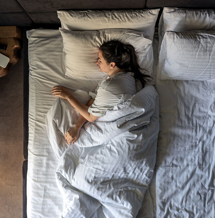Woman lying in bed wrapped in white sheets, illustrating things people only started to believe once it happened to them
