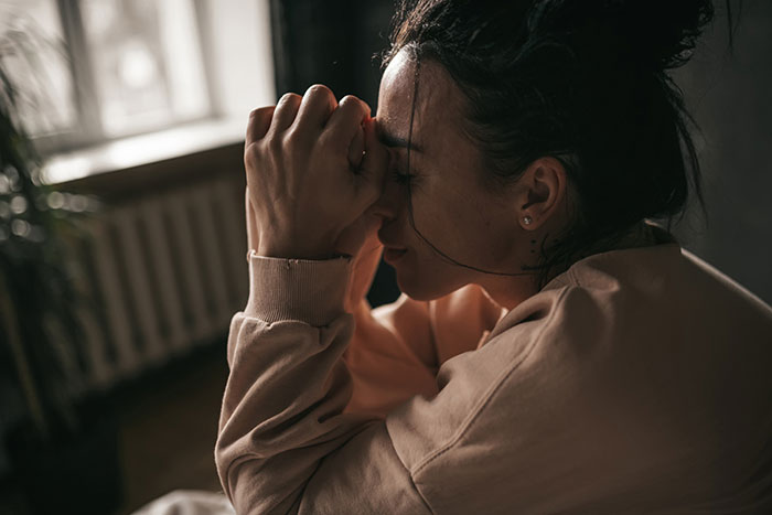 Woman in casual clothes sitting indoors with eyes closed and hands clasped, reflecting on things people only believe once experienced