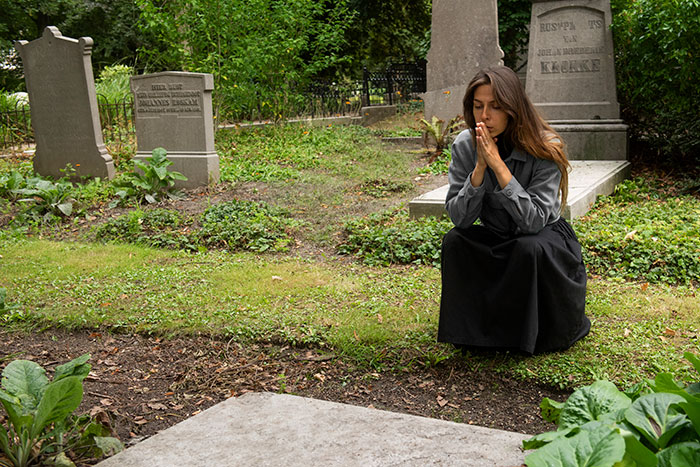Woman praying quietly at a grave in a cemetery, reflecting on experiences people only believe once it happens to them