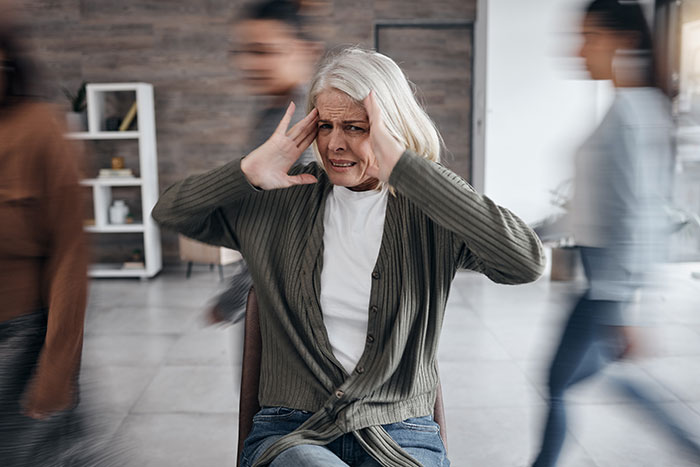 Older woman holding her head in stress, surrounded by blurred people walking fast, illustrating things people believe once experienced.