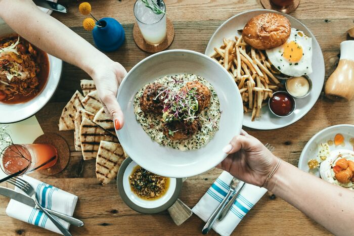 Hands passing a bowl of food over a table with various dishes, illustrating everyday things people accidentally did wrong.