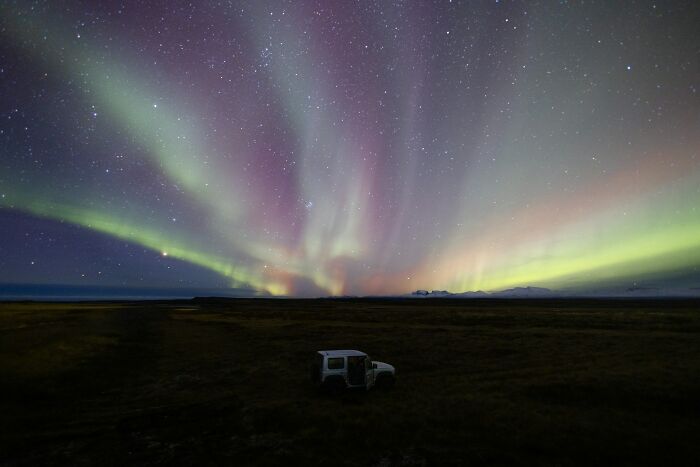 Northern lights display over a dark landscape with a vehicle, illustrating mesmerizing life facts that make you do a double take.