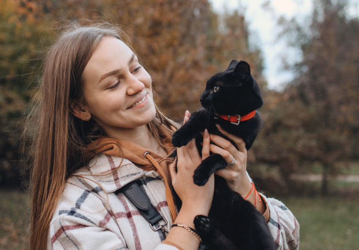 Young woman holding a black cat outdoors, smiling and enjoying a moment, reflecting on stealing wrong cat paying bills concept. Young woman holding a black cat outdoors, smiling and enjoying a moment, reflecting on stealing wrong cat paying bills concept.