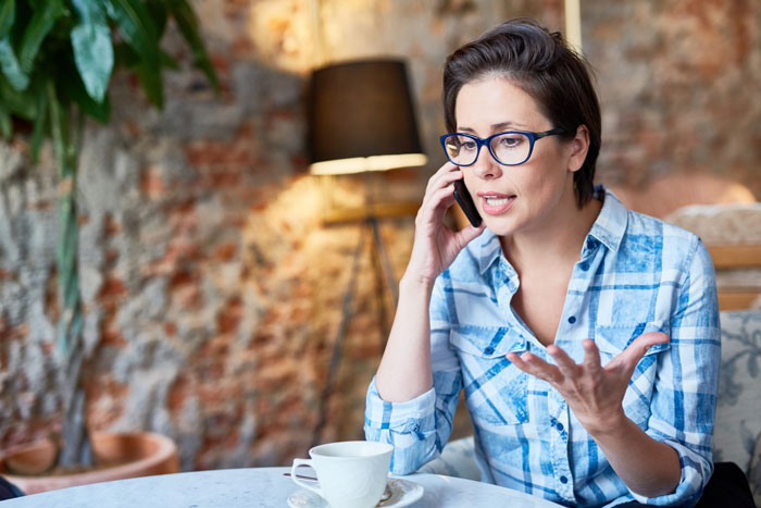 Woman in blue plaid shirt and glasses making a serious phone call about stepmom delivering a brutal reality check.