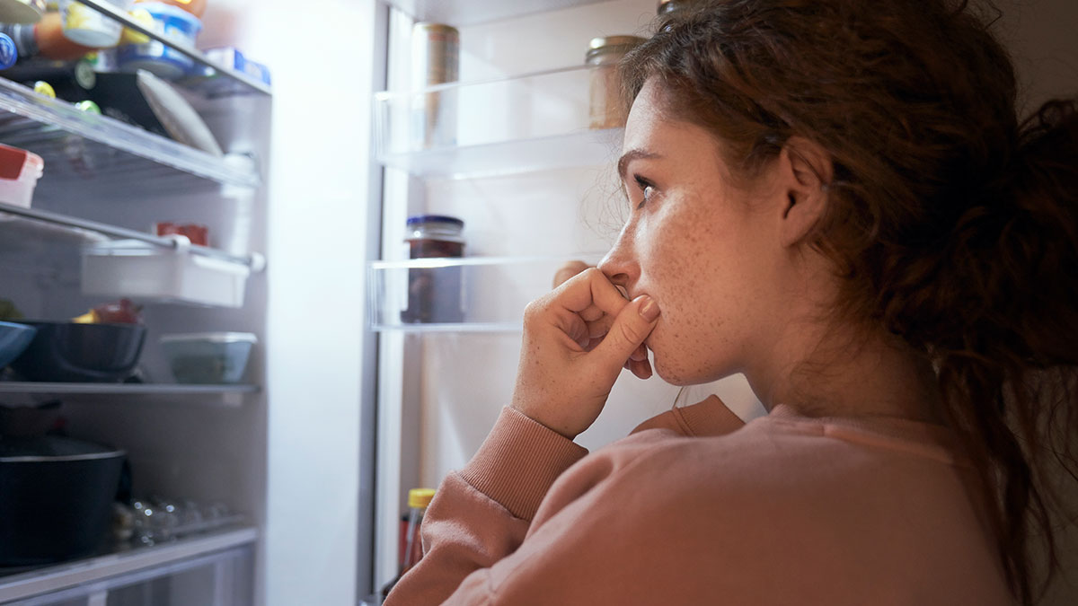 Woman looking shocked at an empty fridge after Thanksgiving family clears leftovers in a kitchen setting.