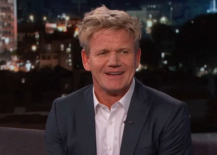 Celebrity smiling in a dark blazer and white shirt during an evening TV interview about their vibes and personality.