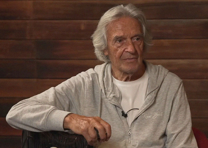 Elderly man with white hair in a gray hoodie sharing vibes of celebrities he has met in a relaxed setting.