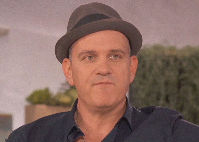 Man wearing a gray hat and dark shirt sitting indoors, sharing experiences about celebrities and the vibes they gave off