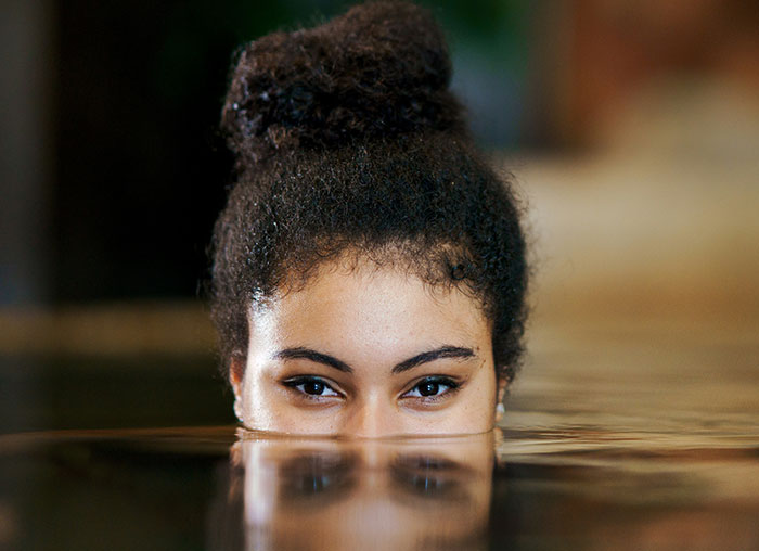 Young woman partially submerged in water, demonstrating the mammalian dive reflex with focused eyes above the surface.