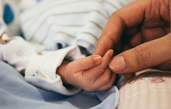 Adult hand gently holding a newborn's hand, illustrating the human body and mammalian dive reflex connection.