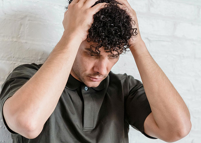 Young man with curly hair holding his head, portraying confusion related to wild and funny post-anesthesia acts.